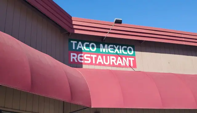 The front of the building on a sunny day: the green and red TACO MEXICO RESTAURANT sign above a maroon awning, under a blue sky