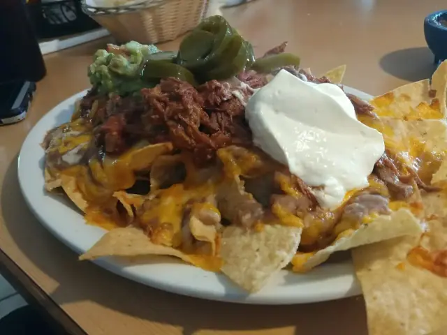 A plate of loaded nachos with melted cheese, shredded meat, jalapenos and sour cream