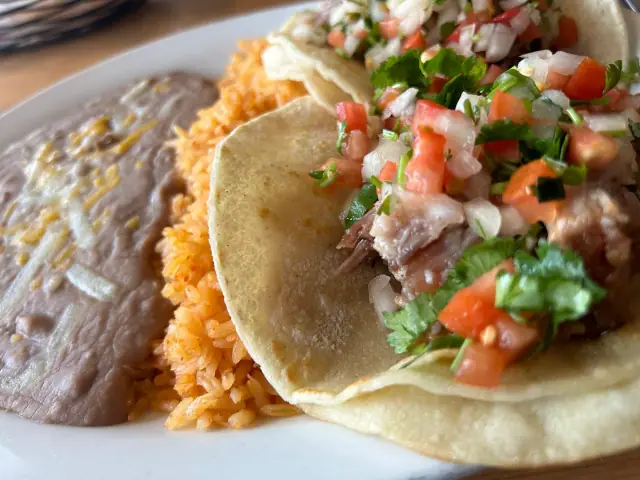 Tacos on corn tortillas topped with pico de gallo, with rice and beans beside them